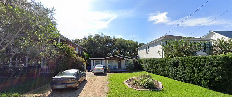 A small, run-down house surrounded by modern townhomes.